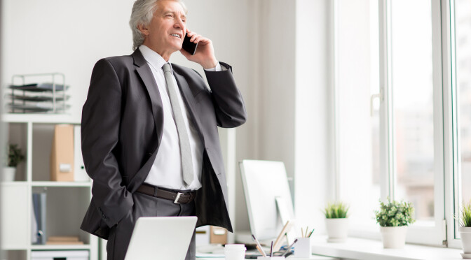 Confident mature businessman with smartphone phoning to one of subordinates by his workplace